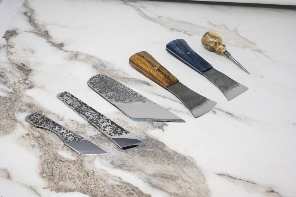 Five crafting tools with distinctive wooden and metal handles are beautifully displayed on a marble surface, forming the perfect March Madness Super Set for any artisan's collection.
