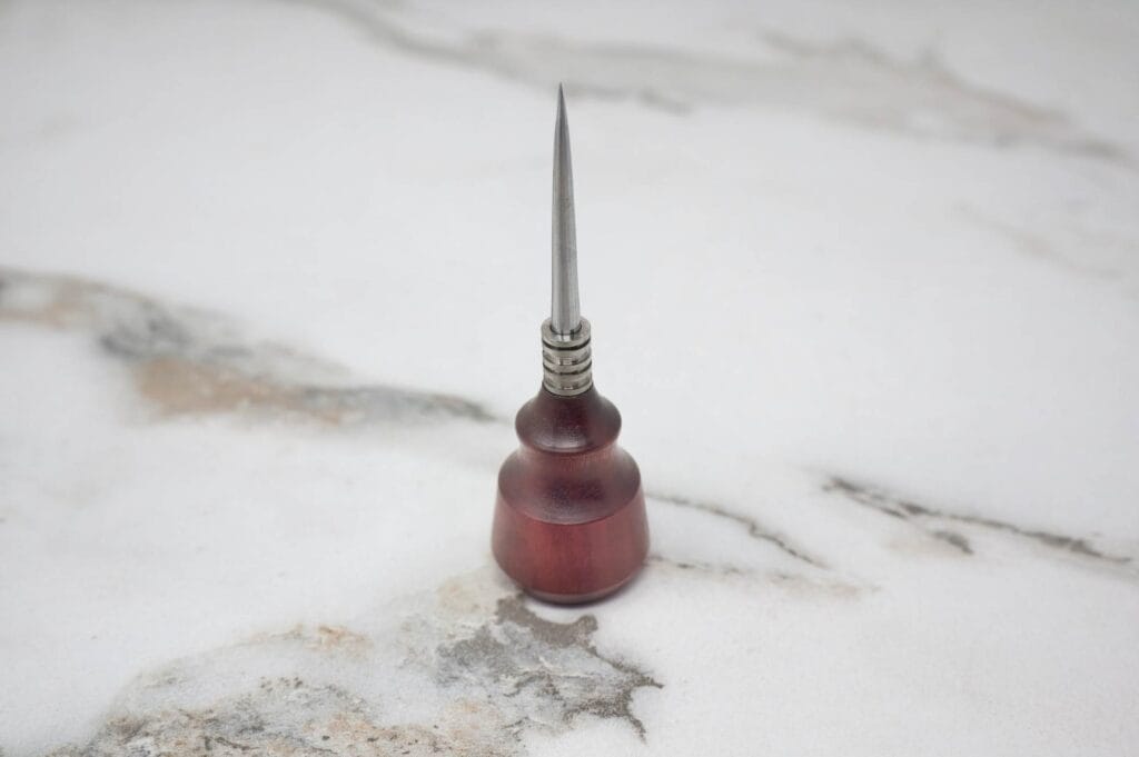 Wooden-handled marlinspike with a metal tip, placed upright on a marble surface.