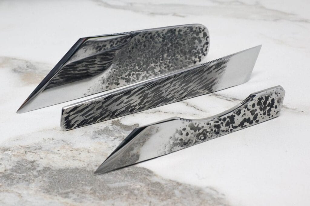 The 3 Piece Super Skiver Set, with three uniquely designed knives showcasing textured blade patterns, is stylishly presented on a marble surface.