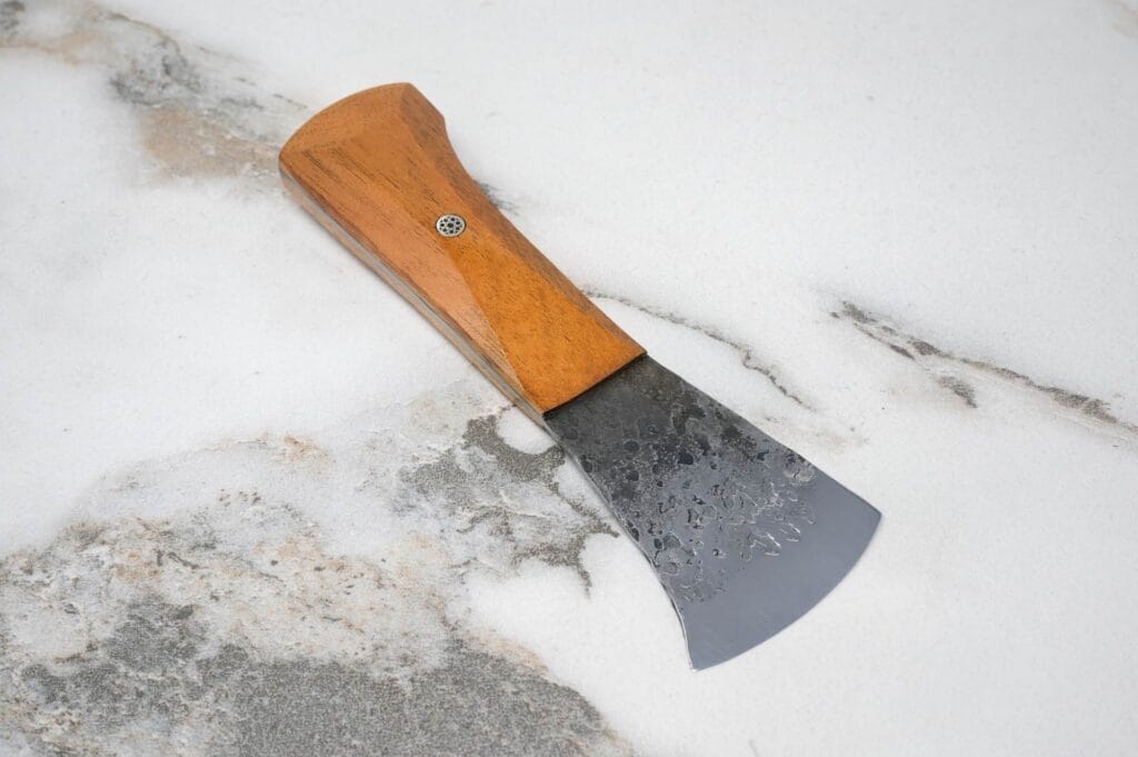 A Forged American Signature Classic hand axe with a wooden handle and metal blade rests on a marble surface, exuding timeless elegance.