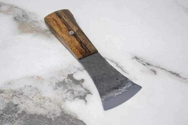A Flat American Signature Leathercraft Knife with a wooden handle elegantly rests on the marbled surface, showcasing its craftsmanship.
