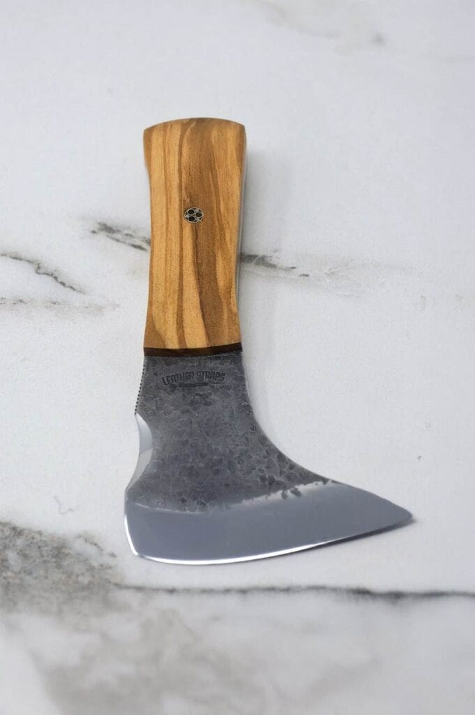 A small, handcrafted knife with a wooden handle and a curved, textured blade rests on a marble surface.