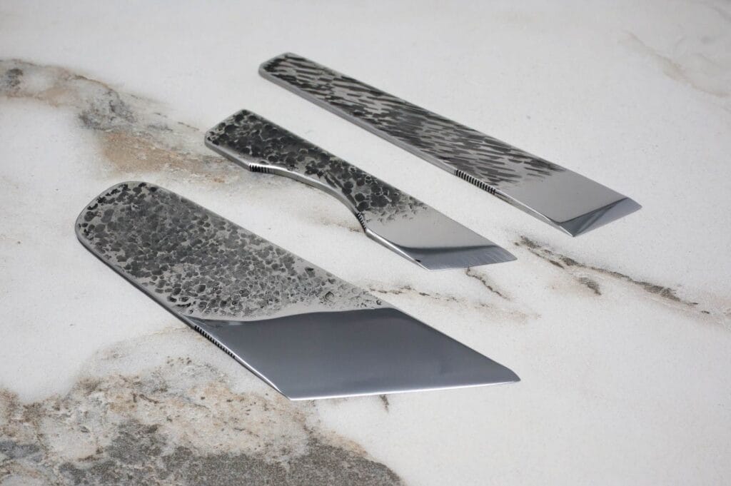 Three polished modern knives with textured handles and blades, displayed on a marble surface.