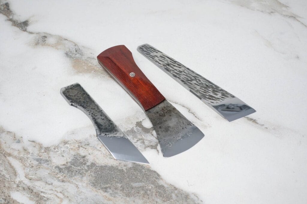 The March Madness 3 Piece Essentials set features three knives with textured metal blades and wooden handles, elegantly displayed on a marble surface.