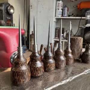 Six Black Palm Leather Awls (Limited Run) with wood handles and metal points are arranged by size on a workbench, tools in the background. This unique set is both functional and eye-catching for any craftsperson.